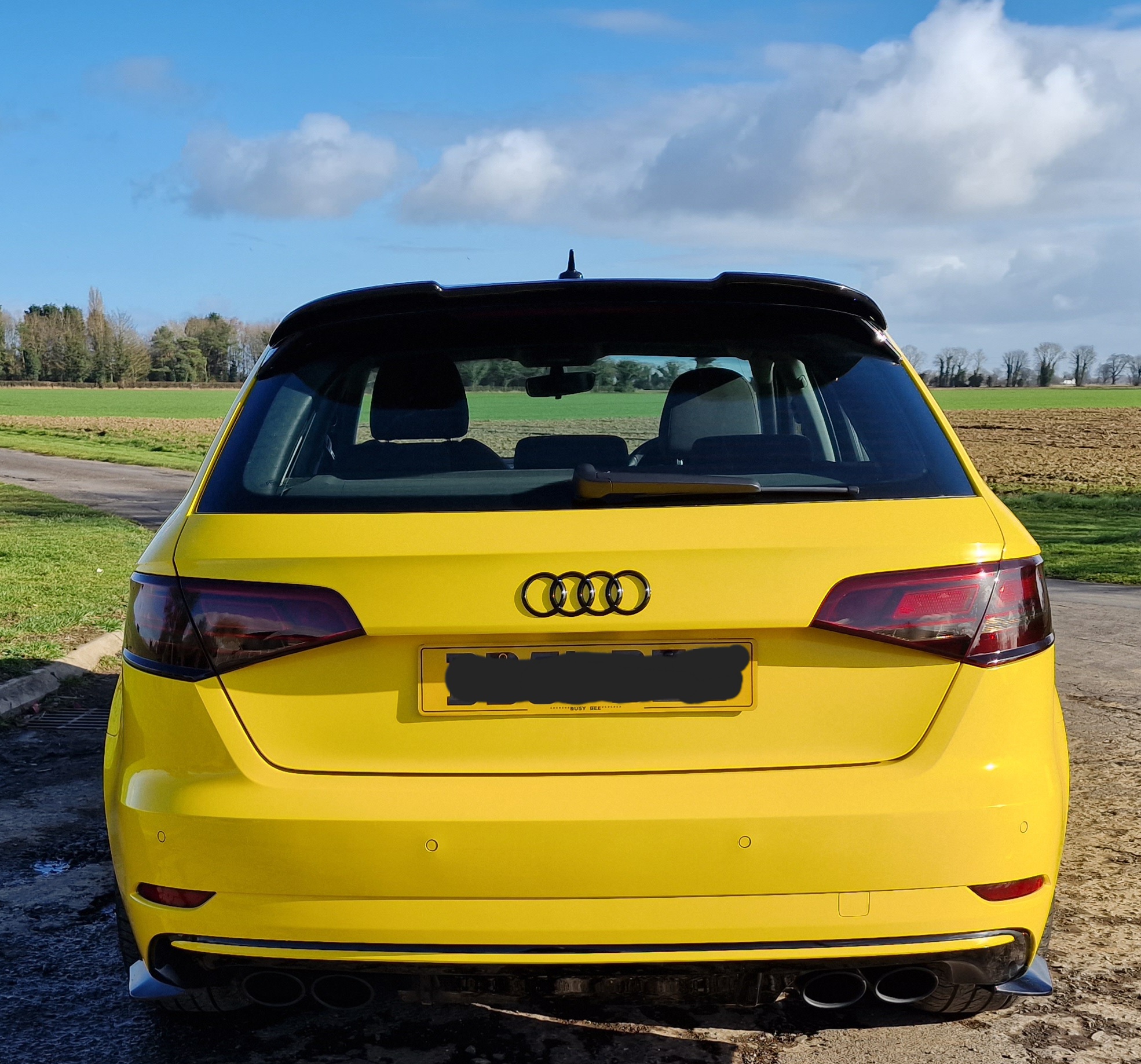 A freshly finished yellow Audi hatchback in the yard under a wide fenland sky
